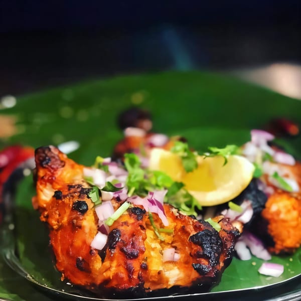 Indian Tandoori chicken, garnished with red onions, cilantro, and a lemon wedge on a banana leaf.
